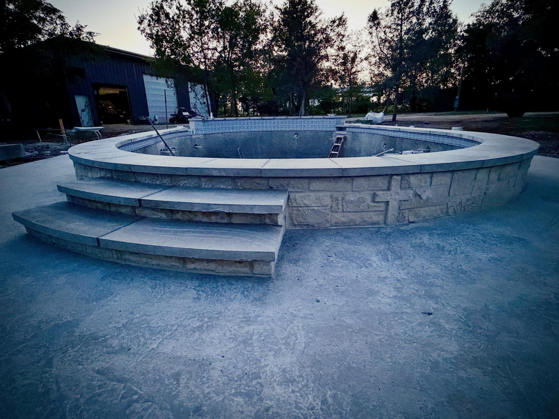 Round stone-clad pool with tile band and broom-finished deck